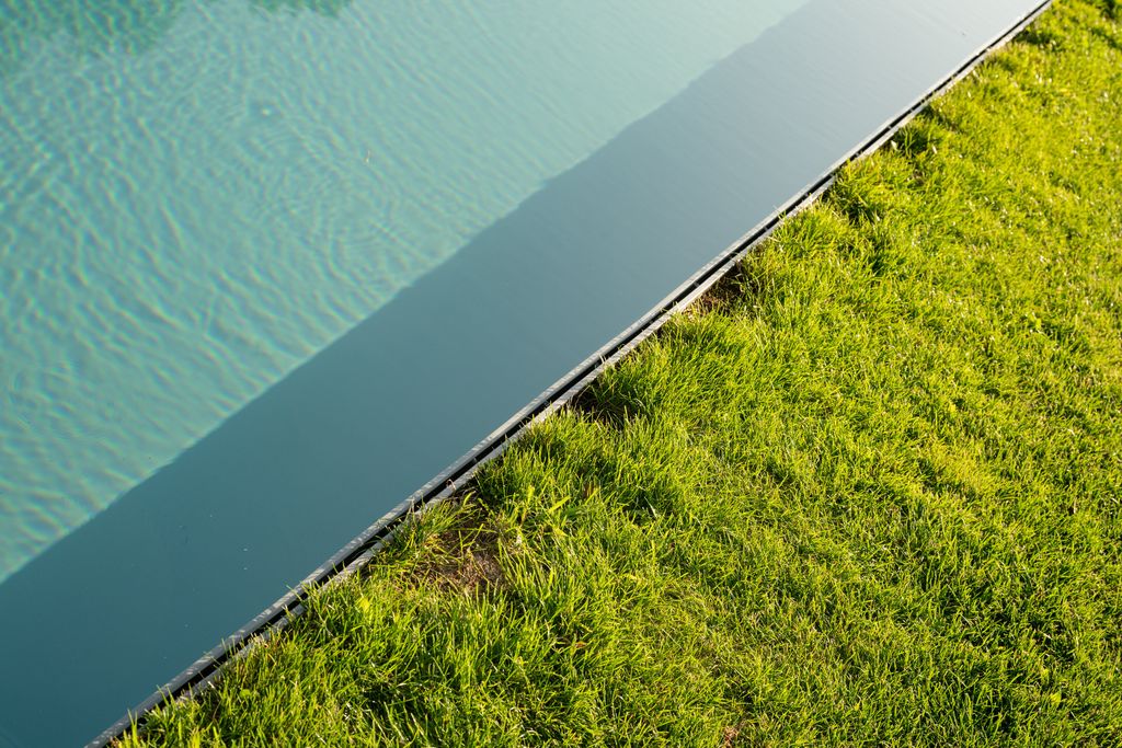Détail du bord de la piscine : la pelouse rejoint la surface de l'eau sur une fine arête métallique
