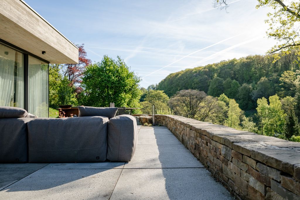 Terrasse en béton bordée d'un muret en pierre naturelle, ouverte sur la vallée boisée