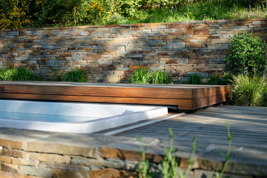 Mur de soutènement en pierre naturelle et terrasse en bois autour d'une piscine à volet en bois, près d'Eupen