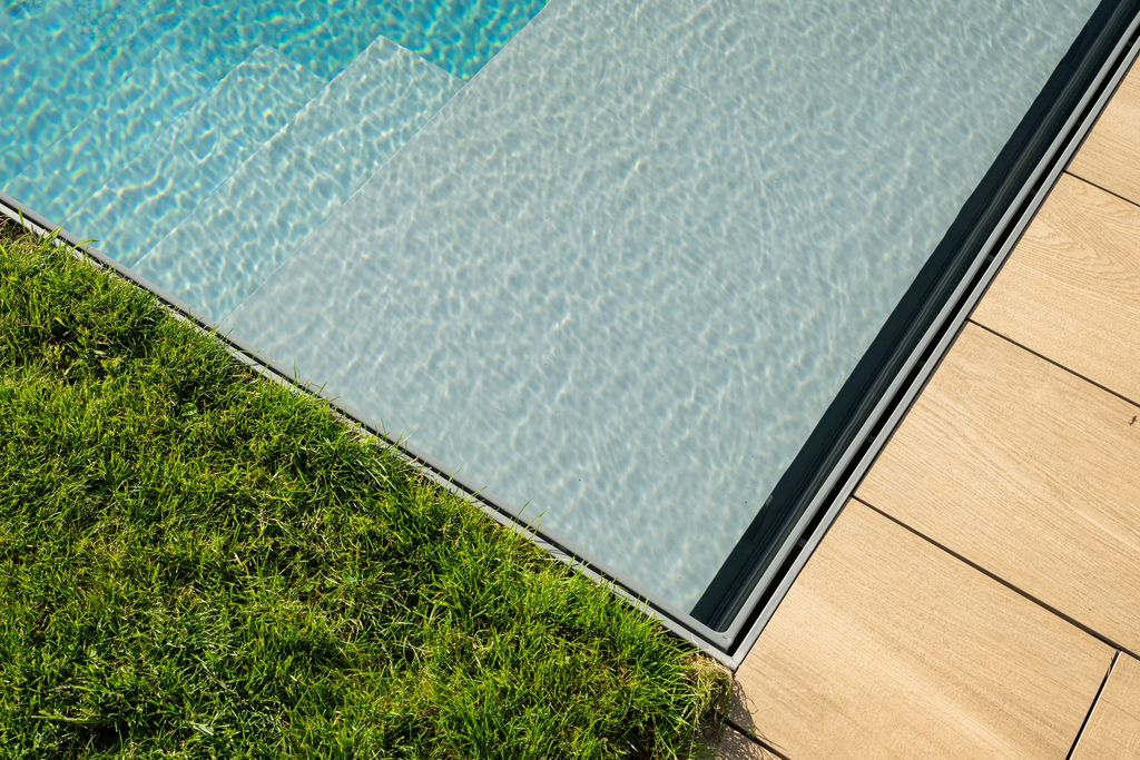 Gros plan sur l'angle de la piscine où le gazon s'arrête directement au bord de l'eau, sans margelle