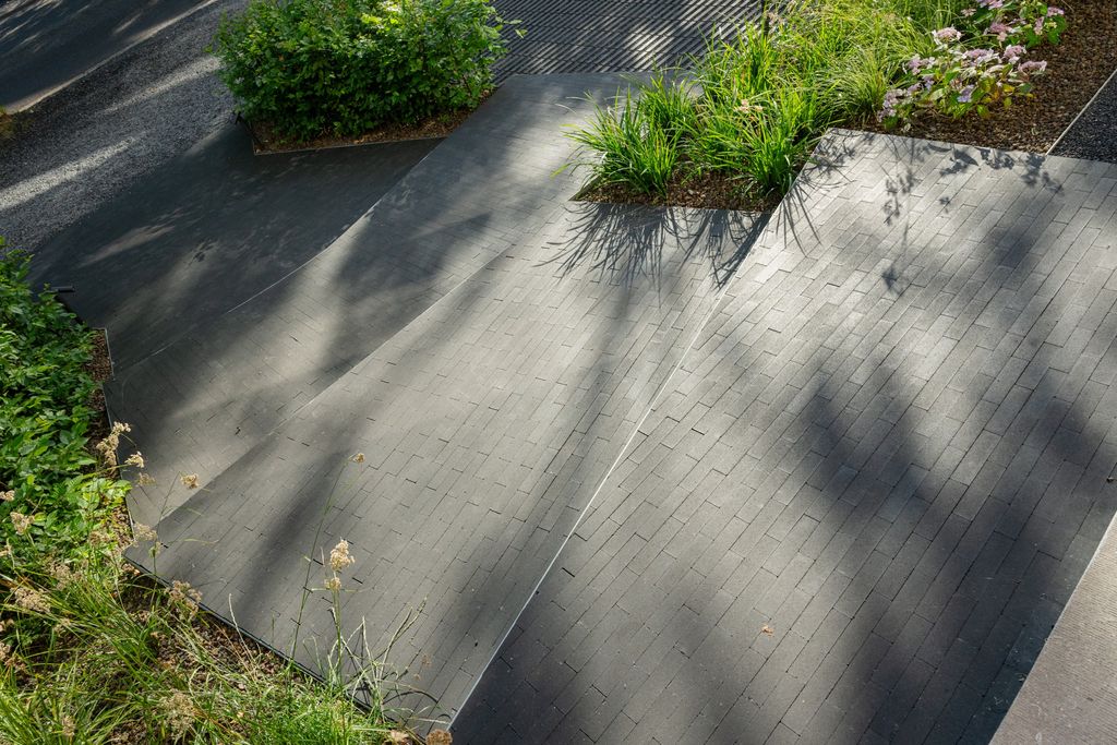 Lignes incurvées en creux et en relief de l'allée pavée, avec ses massifs de graminées, à Verviers