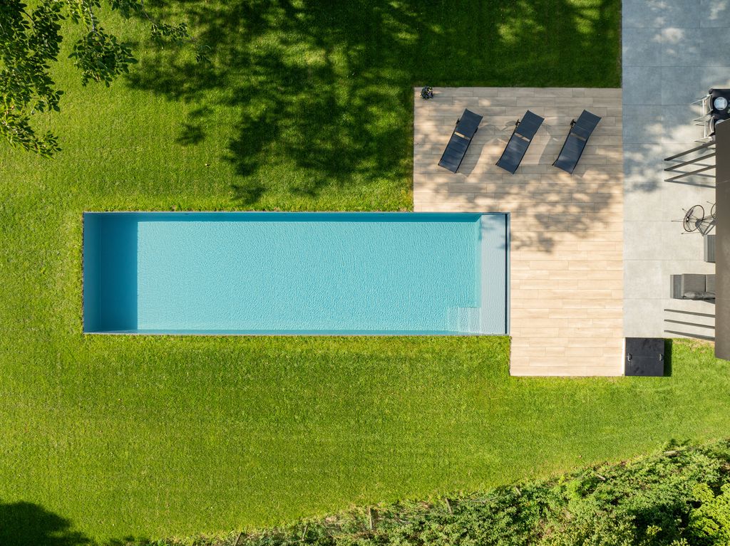 Vue du dessus de la piscine rectangulaire bordée de gazon sur trois côtés et d'une terrasse en bois sur le quatrième