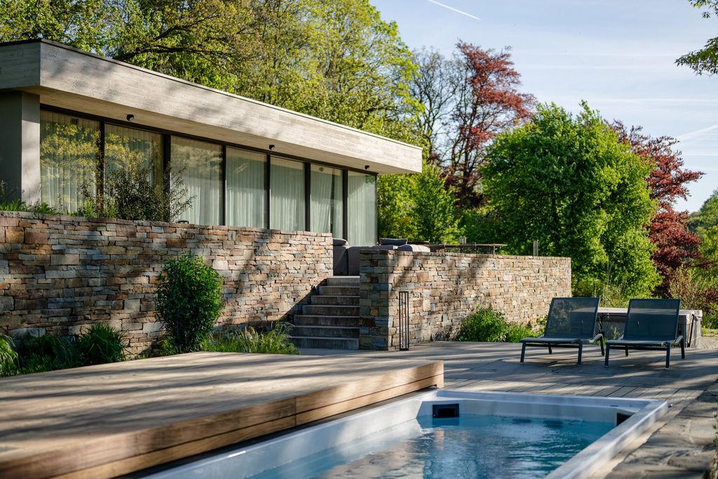 Pavillon vitré à toit plat, terrasse en bois et piscine en contrebas d'un mur en pierre naturelle