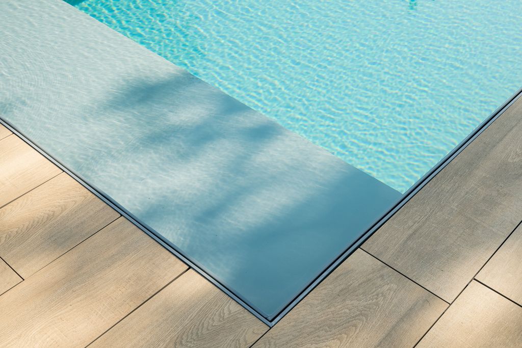 Angle de la piscine à débordement au niveau de la terrasse en bois, l'eau affleurant les lames