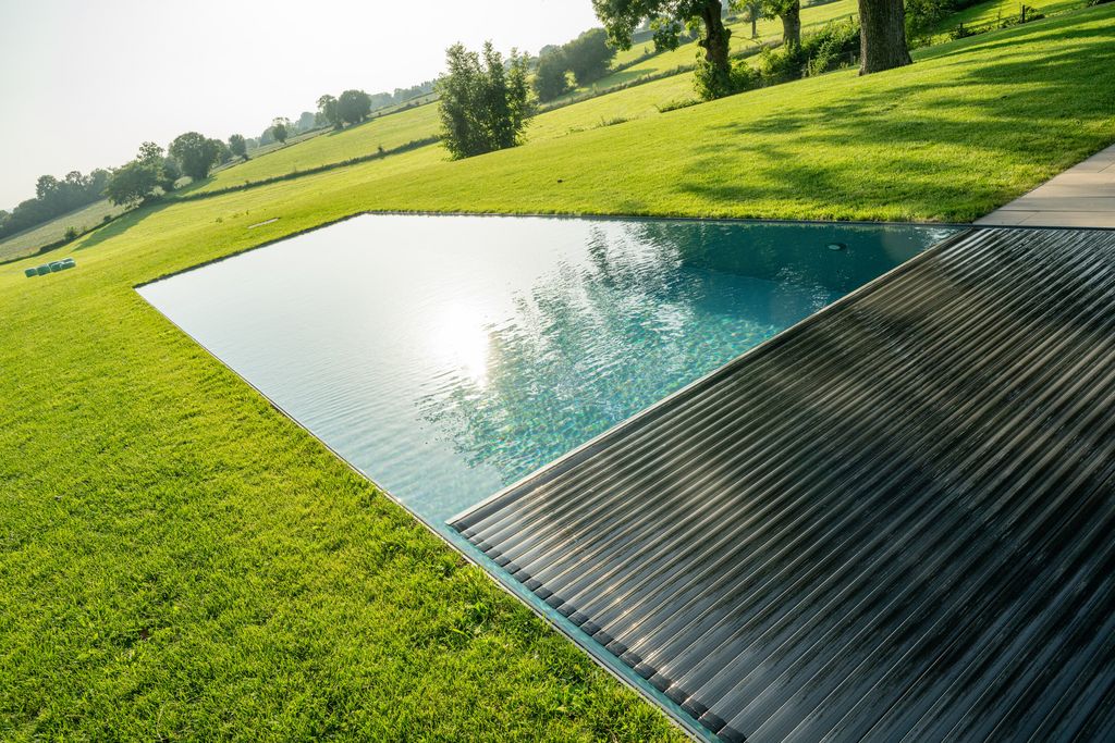 La piscine à moitié recouverte par son volet immergé, encastrée dans la pelouse en pente douce