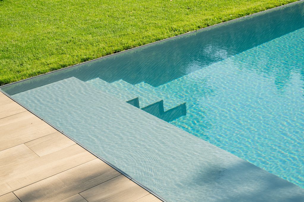 L'escalier immergé de la piscine vu depuis la terrasse, avec le gazon au ras de l'eau en arrière-plan