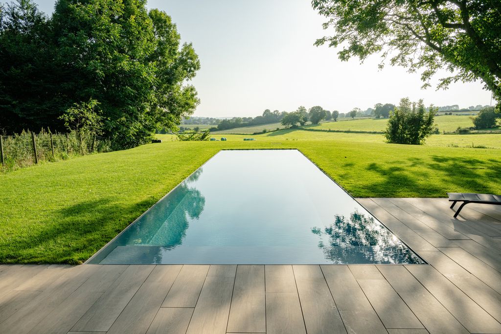 La piscine à débordement vue depuis la terrasse en bois, le gazon filant jusqu'aux prairies de Verviers