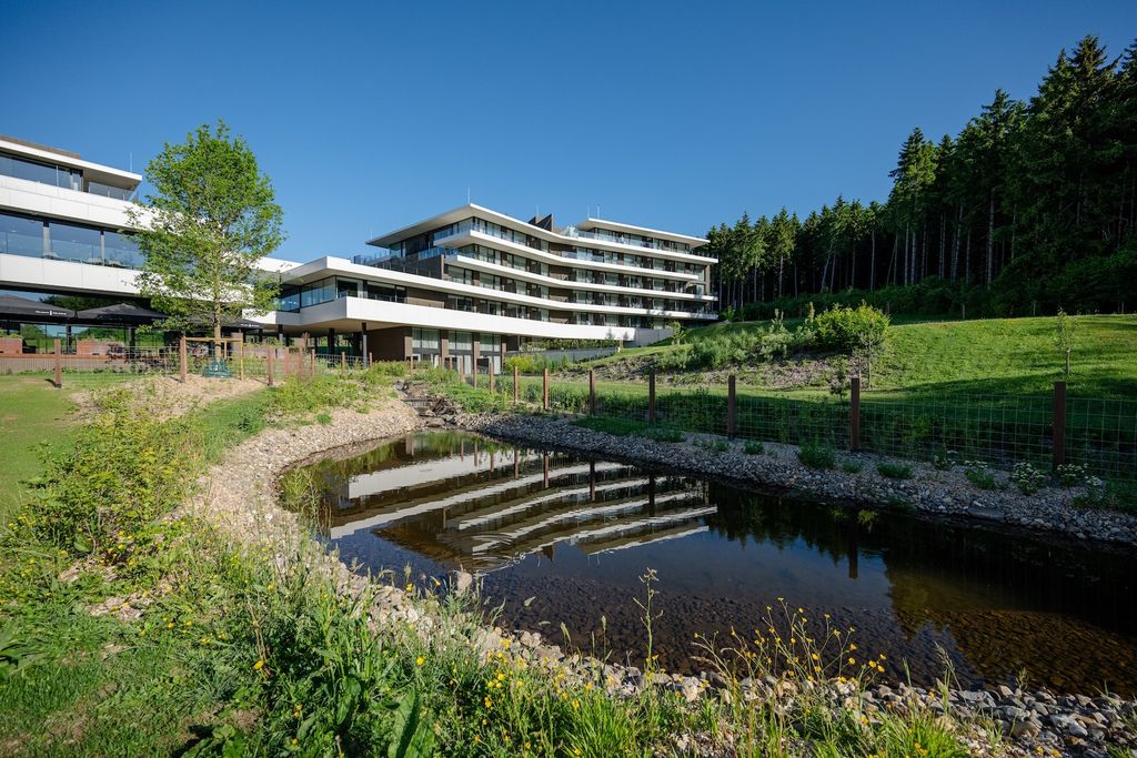 Plan d'eau aux berges de galets devant l'Anatura Hotel & SPA à Weiswampach