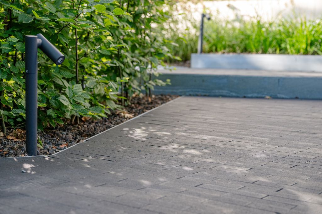 Borne d'éclairage extérieur au pied d'un massif, le long de l'allée pavée en pente, à Verviers