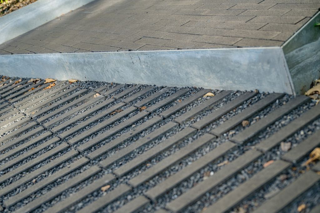 Détail des pavés drainants sur lit de gravier et d'une bordure métallique de l'allée, à Verviers